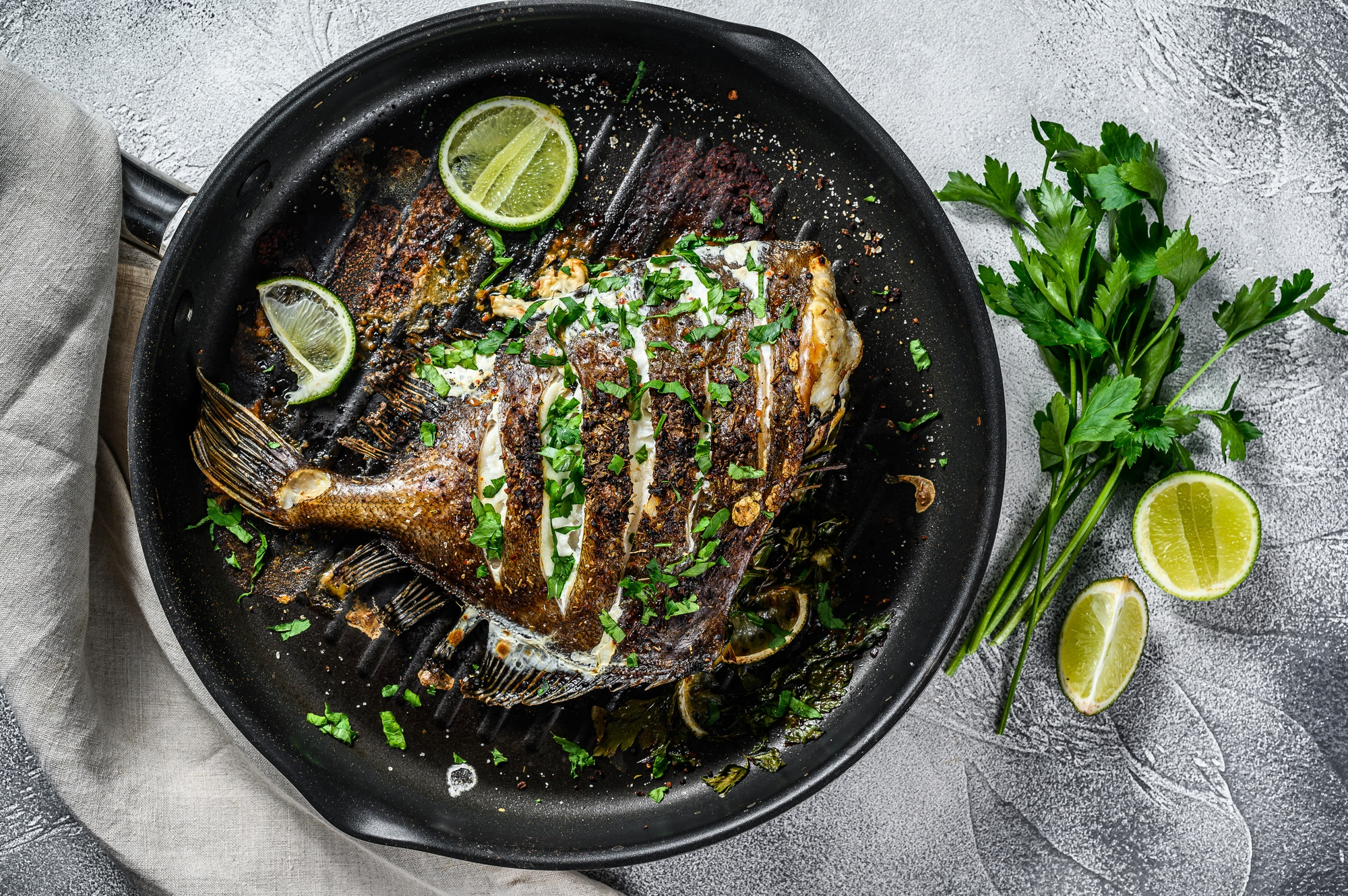 Fried Dory fish with lime and parsley in a pan. Vegatarian health food. Gray background. Top view